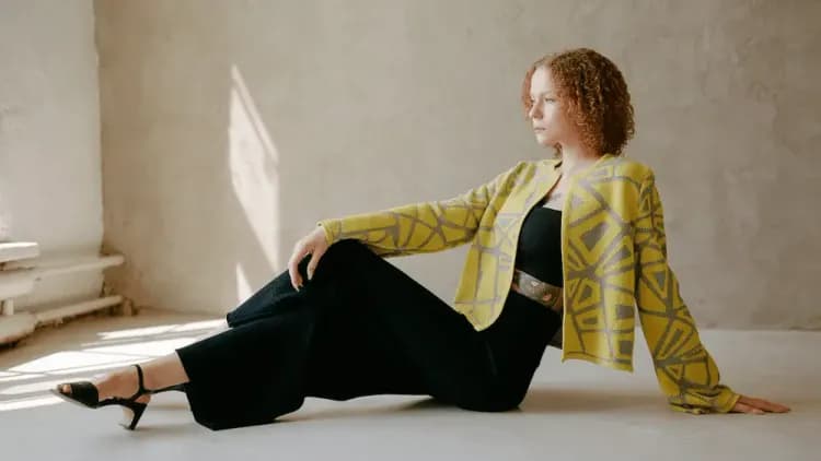 A stylish woman sitting on the ground in a yellow jacket and black dress